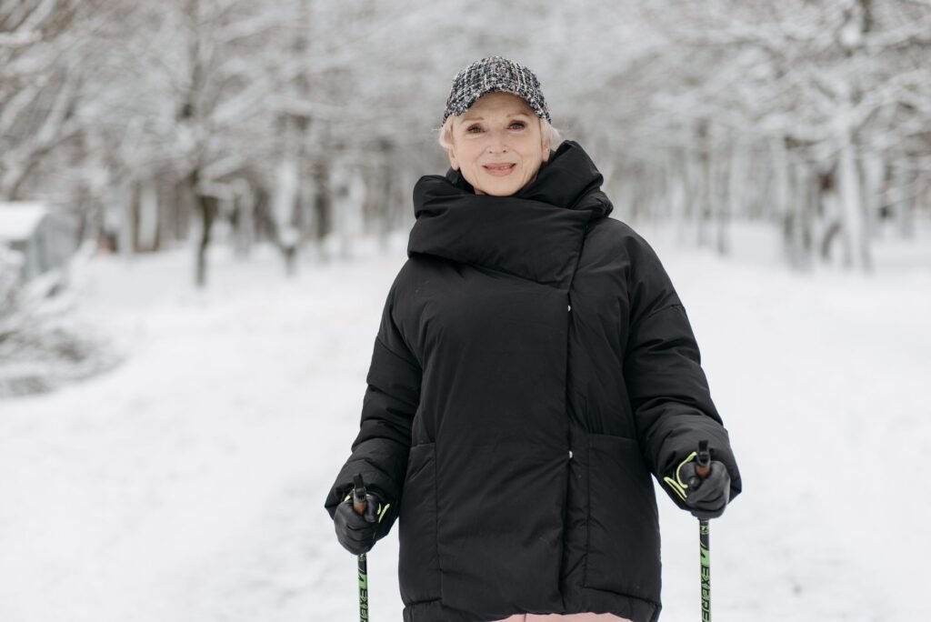 Senior woman enjoying a winter walk with ski poles in a snowy park, dressed in warm attire